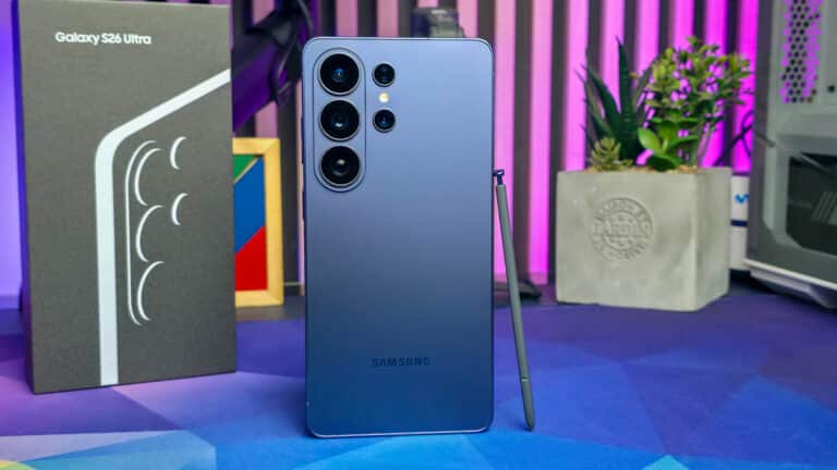 Vista trasera del Samsung Galaxy S26 Ultra mostrando su módulo de cámaras múltiples, acompañado del S Pen y su caja, en un entorno de escritorio con luces LED y decoración