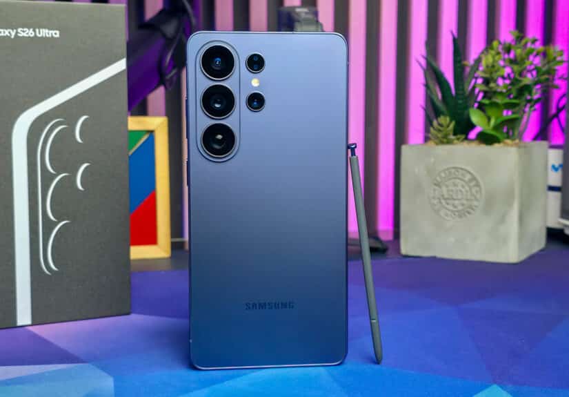 Vista trasera del Samsung Galaxy S26 Ultra mostrando su módulo de cámaras múltiples, acompañado del S Pen y su caja, en un entorno de escritorio con luces LED y decoración